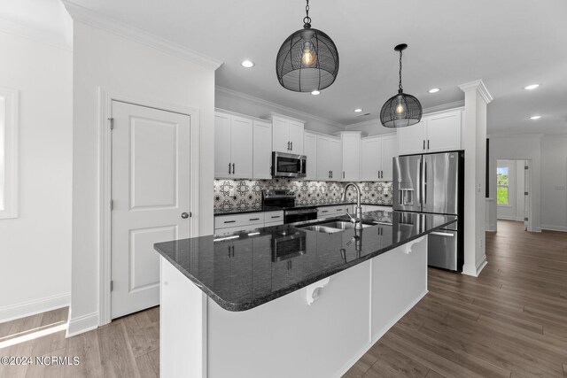 kitchen with white cabinets, decorative backsplash, ornamental molding, stainless steel appliances, and a sink