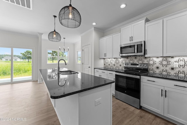 kitchen with decorative backsplash, appliances with stainless steel finishes, a kitchen island with sink, crown molding, and a sink