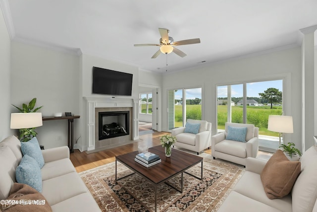 living room with light wood-style floors, a tile fireplace, ornamental molding, and ceiling fan