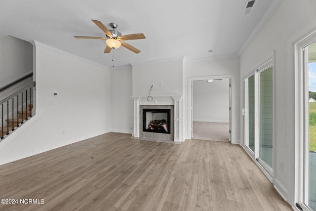 unfurnished living room with light wood finished floors, a tiled fireplace, ornamental molding, ceiling fan, and stairs