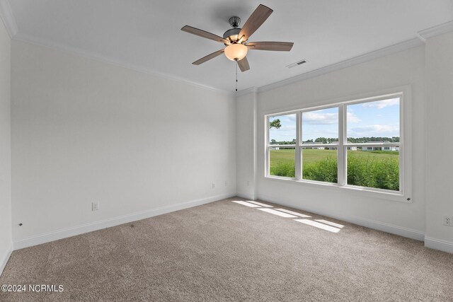 carpeted spare room featuring baseboards, a ceiling fan, visible vents, and crown molding