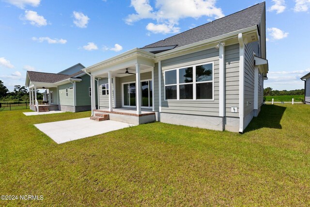 back of house with a ceiling fan, a lawn, a shingled roof, and a patio