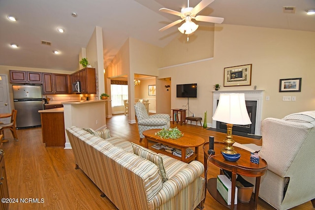 living room with ceiling fan, light wood-type flooring, and high vaulted ceiling