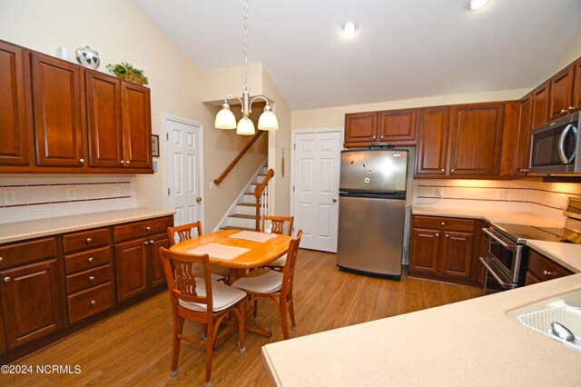 kitchen featuring pendant lighting, backsplash, an inviting chandelier, light wood-type flooring, and appliances with stainless steel finishes