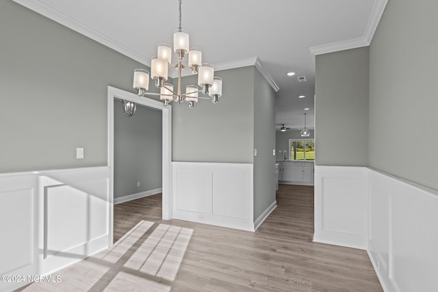 unfurnished dining area featuring ceiling fan with notable chandelier, crown molding, and light hardwood / wood-style flooring