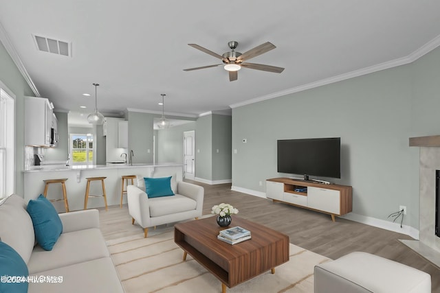 living room with a high end fireplace, light wood-type flooring, ceiling fan, and crown molding