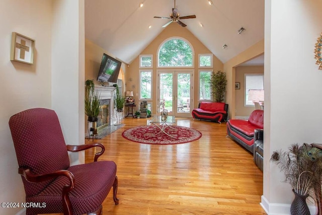 living area with high vaulted ceiling, a premium fireplace, visible vents, french doors, and light wood-type flooring