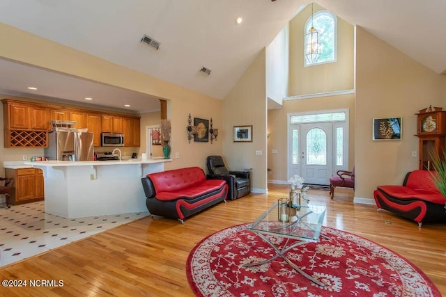 living area featuring high vaulted ceiling, light wood-type flooring, visible vents, and baseboards