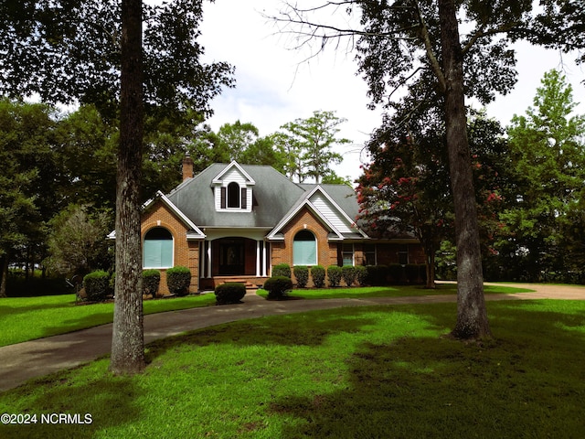 view of front of property featuring a front yard, brick siding, driveway, and a chimney