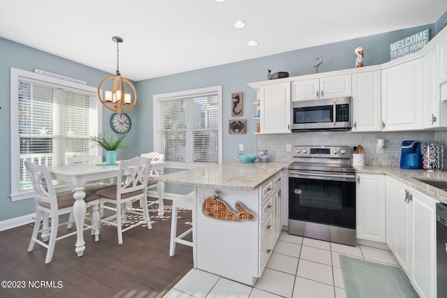 kitchen with white cabinetry, a kitchen breakfast bar, hanging light fixtures, light stone counters, and stainless steel appliances