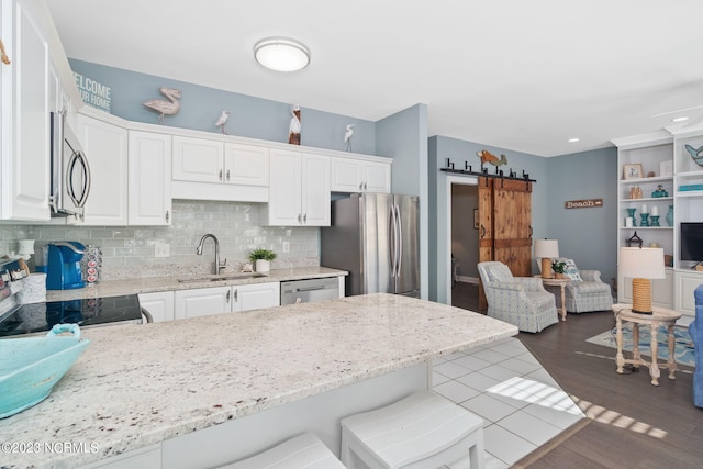 kitchen with a breakfast bar, sink, appliances with stainless steel finishes, a barn door, and white cabinets