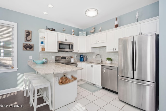 kitchen with a breakfast bar area, tasteful backsplash, kitchen peninsula, stainless steel appliances, and white cabinets