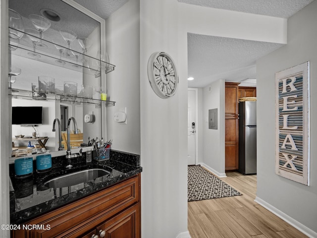 bar with dark stone countertops, stainless steel fridge, sink, and a textured ceiling