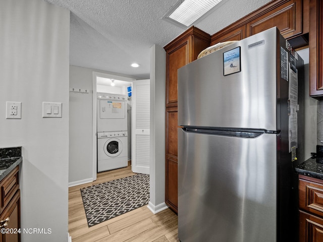 kitchen with stacked washer / dryer, stainless steel fridge, dark stone countertops, a textured ceiling, and light wood-type flooring