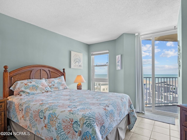 tiled bedroom featuring access to exterior, a water view, and a textured ceiling