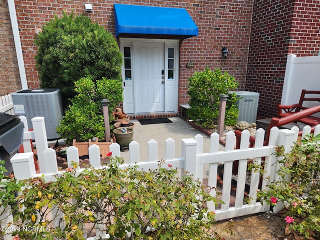 view of exterior entry featuring central air condition unit, fence, and brick siding