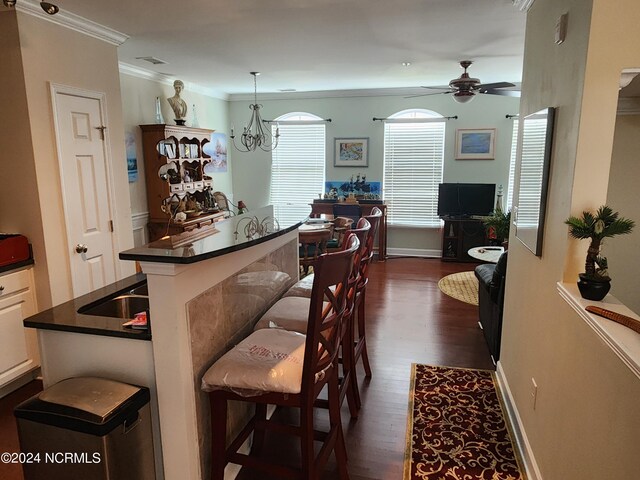 bar with ceiling fan with notable chandelier, dark wood-type flooring, baseboards, ornamental molding, and decorative light fixtures