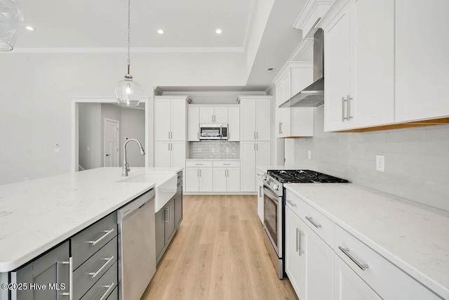 kitchen with wall chimney range hood, appliances with stainless steel finishes, light stone countertops, white cabinets, and decorative light fixtures