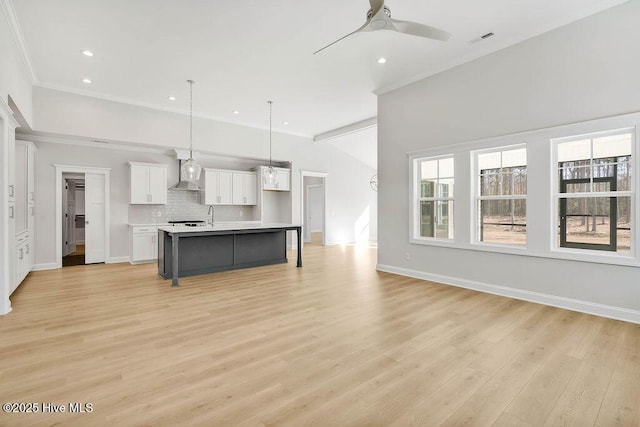 kitchen featuring tasteful backsplash, white cabinets, a center island with sink, decorative light fixtures, and wall chimney exhaust hood