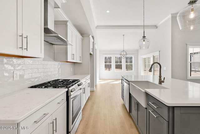 kitchen featuring pendant lighting, wall chimney range hood, sink, a kitchen island with sink, and gas range