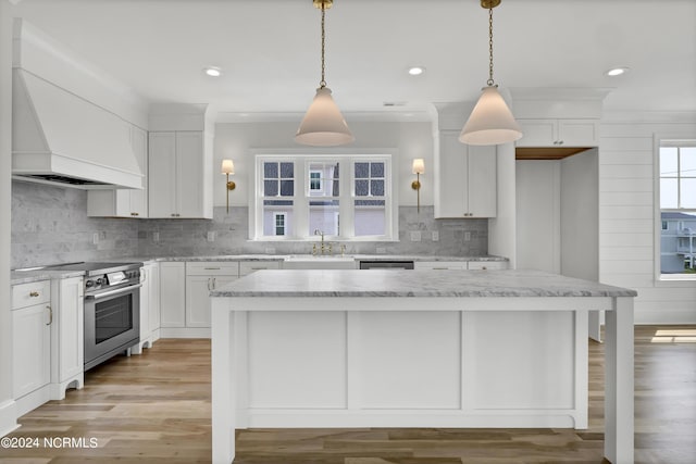 kitchen featuring premium range hood, a center island, white cabinetry, appliances with stainless steel finishes, and light wood finished floors