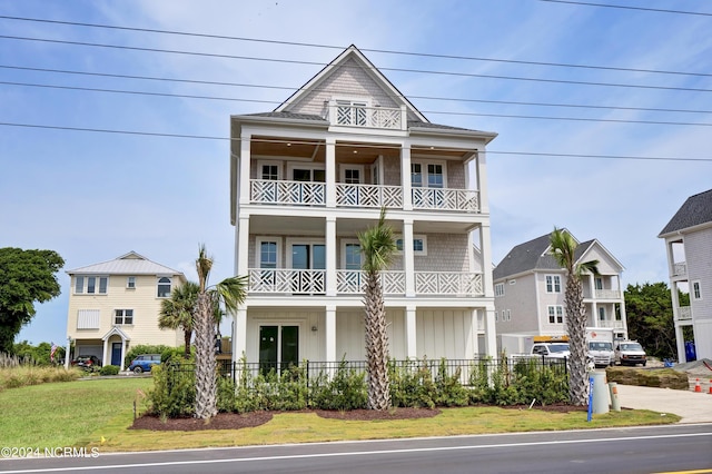 view of front facade with a balcony, board and batten siding, a front yard, and fence