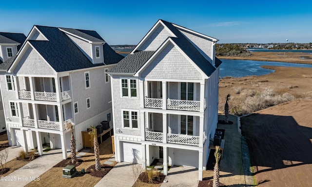 rear view of property with an attached garage, a shingled roof, a balcony, and a water view