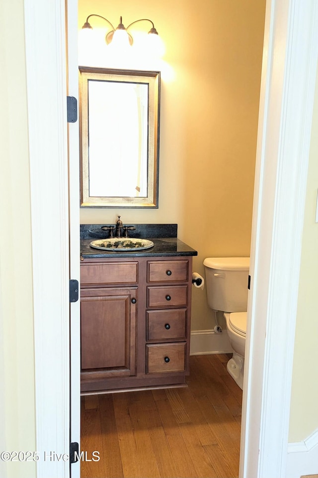 half bath with vanity, wood finished floors, toilet, and baseboards