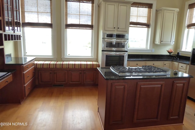 kitchen featuring light wood-style flooring, dark stone countertops, a center island, stainless steel appliances, and cream cabinetry