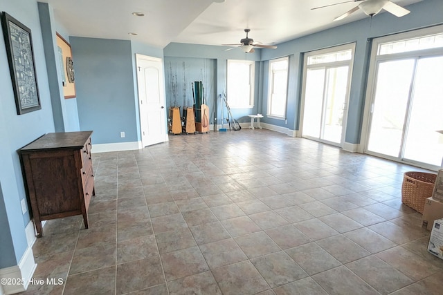 unfurnished living room with tile patterned flooring, a ceiling fan, and baseboards