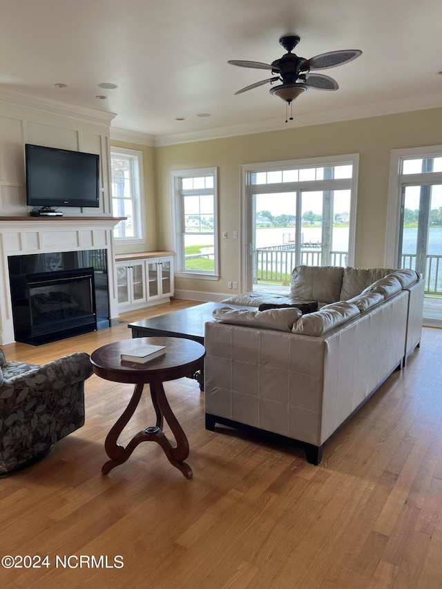 living area with light wood-style floors, plenty of natural light, a glass covered fireplace, and crown molding