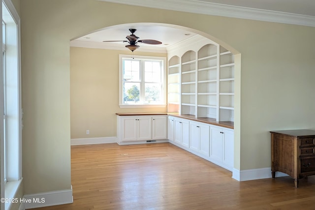 interior space with crown molding, light wood-type flooring, a ceiling fan, and baseboards