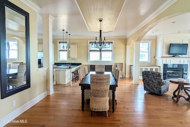 dining space with baseboards, a glass covered fireplace, wood finished floors, and crown molding