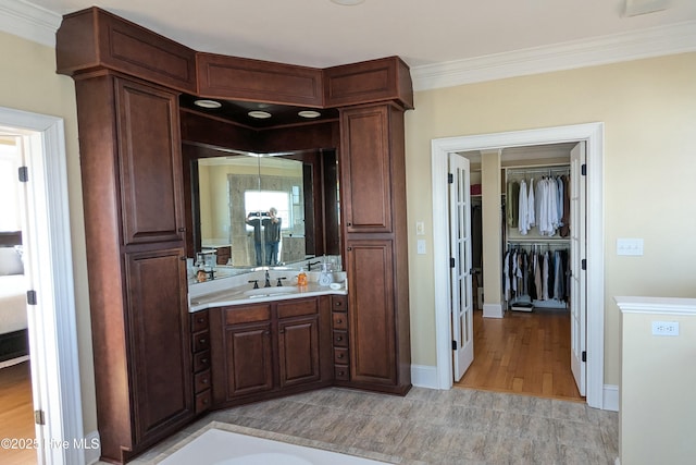 bathroom with baseboards, wood finished floors, crown molding, and vanity