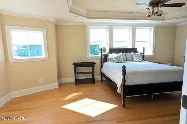 bedroom featuring light wood finished floors, baseboards, a tray ceiling, and crown molding