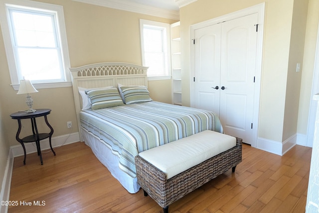 bedroom featuring ornamental molding, a closet, light wood-style flooring, and baseboards