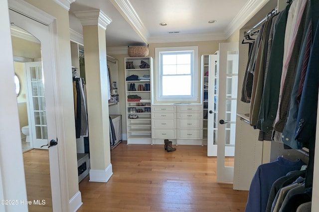 spacious closet with french doors, light wood finished floors, decorative columns, and visible vents