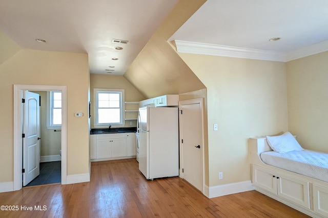 unfurnished bedroom with light wood-type flooring, freestanding refrigerator, a sink, and lofted ceiling