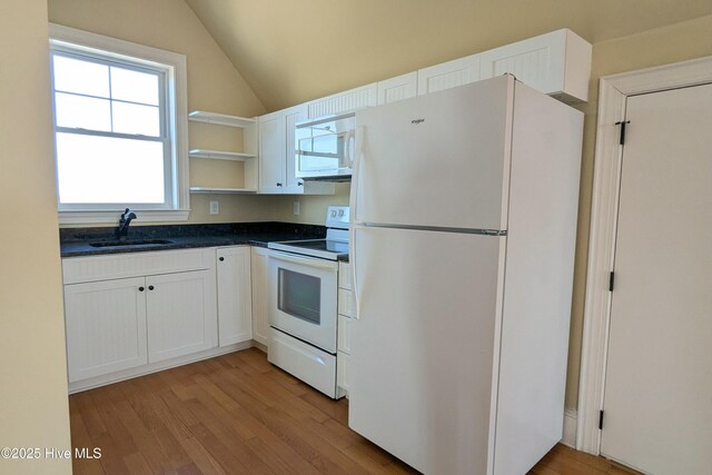 kitchen with lofted ceiling, white appliances, a sink, light wood-type flooring, and dark countertops