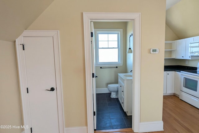 bathroom with toilet, wood finished floors, vanity, baseboards, and vaulted ceiling