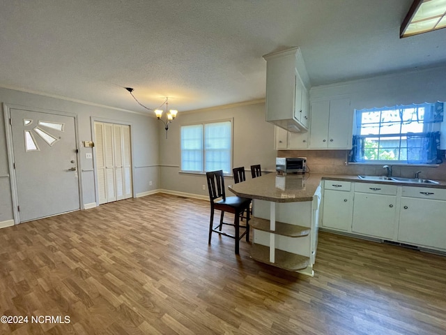 kitchen with ornamental molding, a sink, a textured ceiling, wood finished floors, and a chandelier