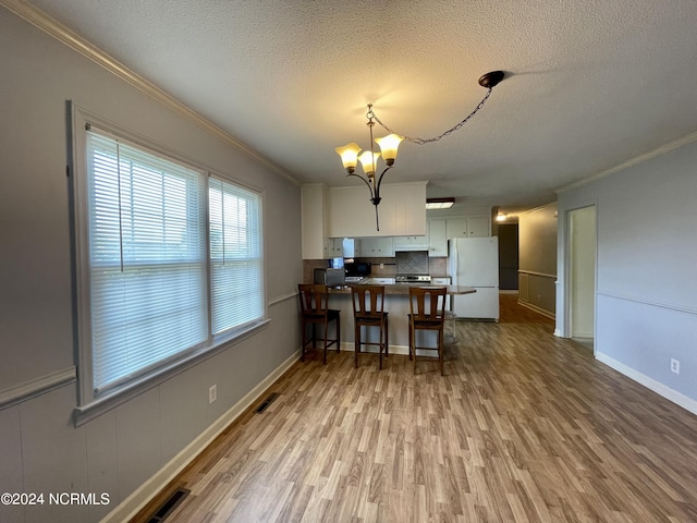 kitchen featuring wood finished floors, freestanding refrigerator, a peninsula, crown molding, and a notable chandelier