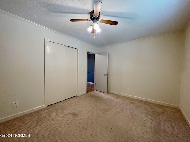 unfurnished bedroom with crown molding, a closet, light carpet, ceiling fan, and baseboards