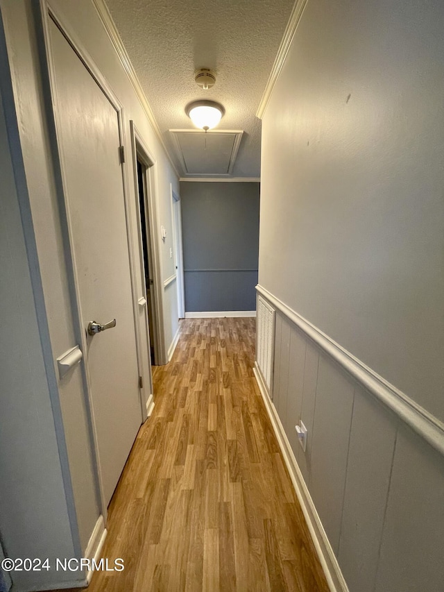 hall with a wainscoted wall, crown molding, attic access, a textured ceiling, and wood finished floors