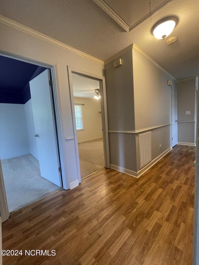 empty room with a textured ceiling, wood finished floors, visible vents, and crown molding