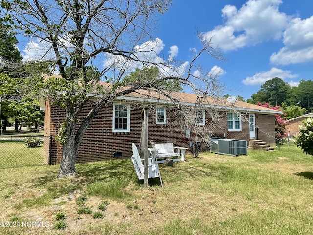 rear view of house with central air condition unit, a yard, fence, and brick siding