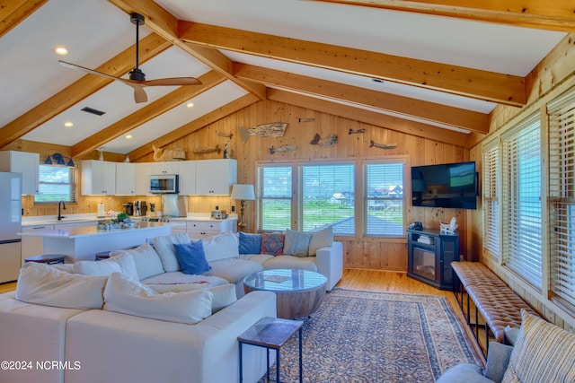 living room featuring wood walls, lofted ceiling with beams, sink, ceiling fan, and light wood-type flooring