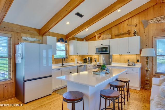 kitchen with stainless steel appliances, sink, lofted ceiling with beams, white cabinets, and a center island