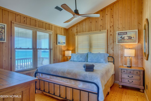 bedroom featuring ceiling fan, light hardwood / wood-style flooring, wood walls, and lofted ceiling