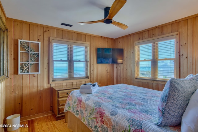 bedroom with light hardwood / wood-style floors, multiple windows, wood walls, and ceiling fan